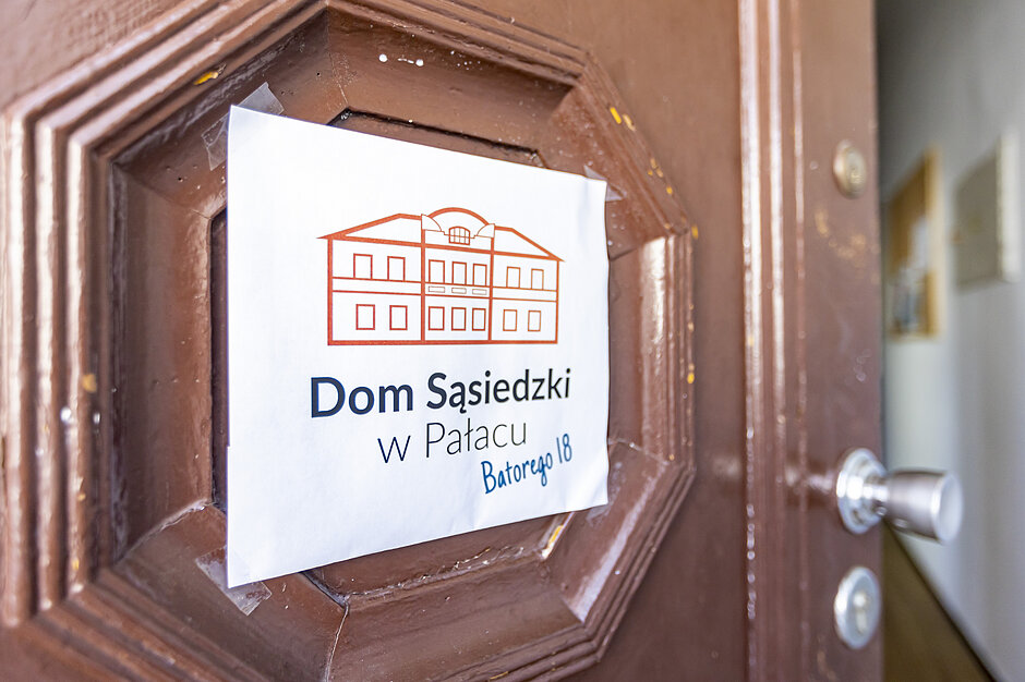Dom Sąsiedzki w Pałacu - zbliżenie na tabliczkę wiszącą na drzwiach