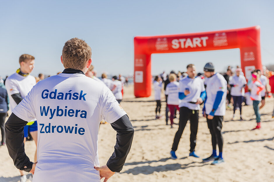 Gdańsk Biega i Wybiera Zdrowie - zbliżenie na mężczyznę w białej koszulce z napisem Gdańsk Wybiera Zdrowie 