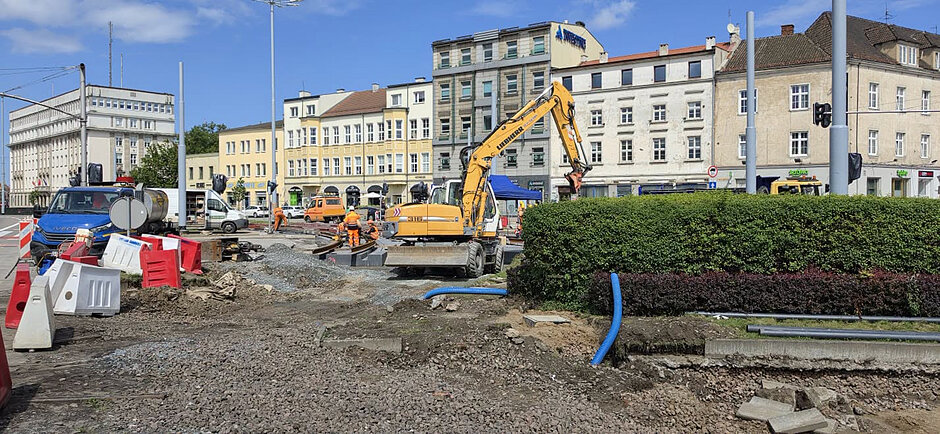remont ulicy w mieście, na zdjęciu maszyna budowlana, w tle budynki i ulica z zerwaną nawierzchnią