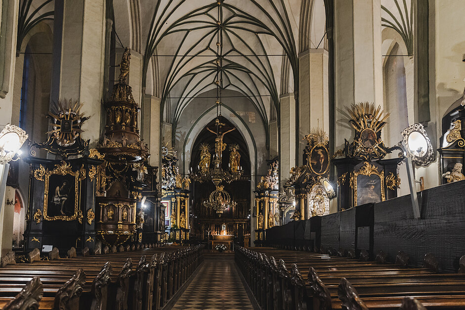 Wnętrze kościoła z wysokimi sufitami i łukami; ściany są pomalowane na biało, a podłoga wykonana jest z czarno-białych kafelków, z których każda jest widoczna z dużym żyrandolem i posągiem Jezusa Chrystusa w środku; na ścianach znajduje się również kilka dużych luster i innych przedmiotów religijnych, w tym posągi świętych i aniołów.