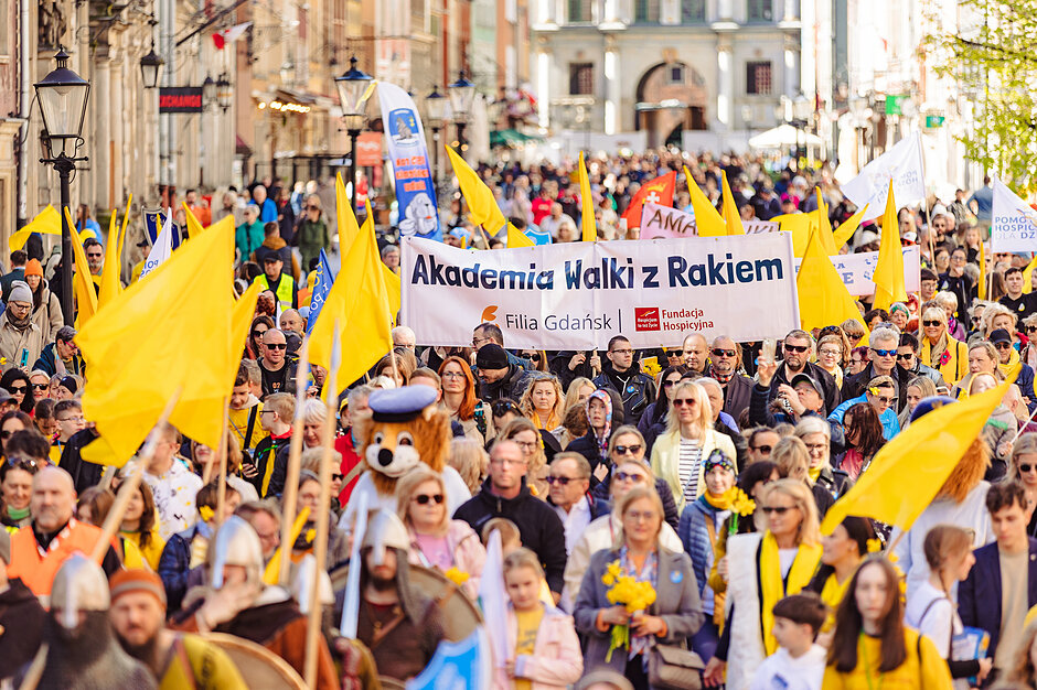 Przemarsz ludzi z żółtymi flagami. Niosą baner Akademia Walki z Rakiem 