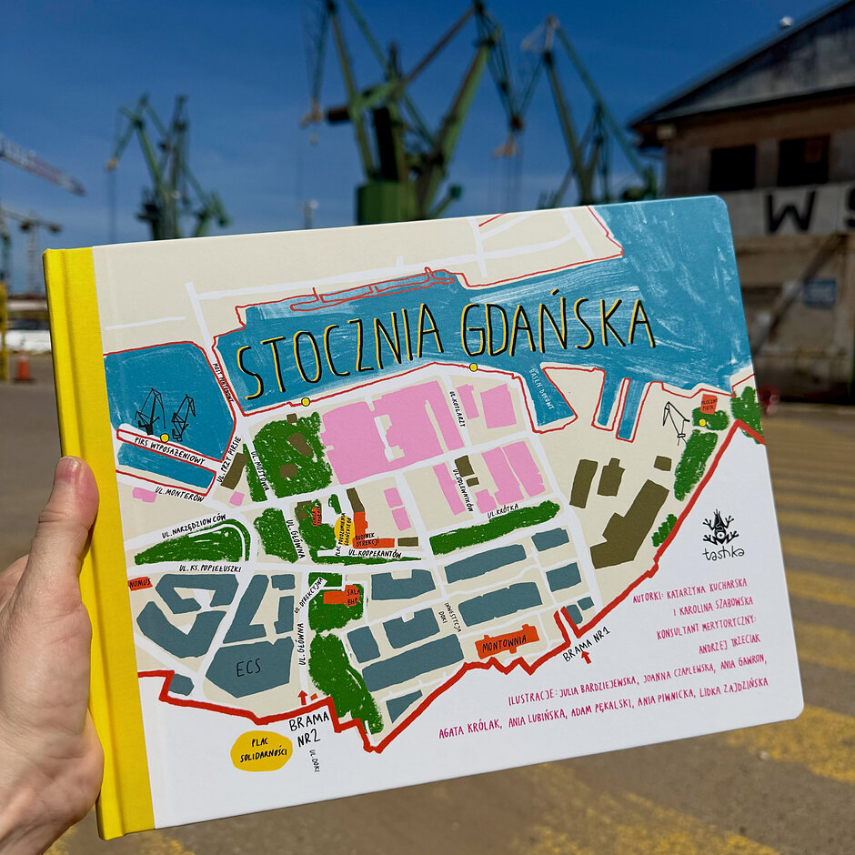 Zdjęcie przedstawia okładkę ilustrowanej książki dla dzieci zatytułowanej „Stocznia Gdańska”, wydanej przez wydawnictwo Tashka. Na pierwszym planie widoczna jest kolorowa mapa terenów stoczniowych z zaznaczonymi obiektami, takimi jak Europejskie Centrum Solidarności czy historyczne bramy.