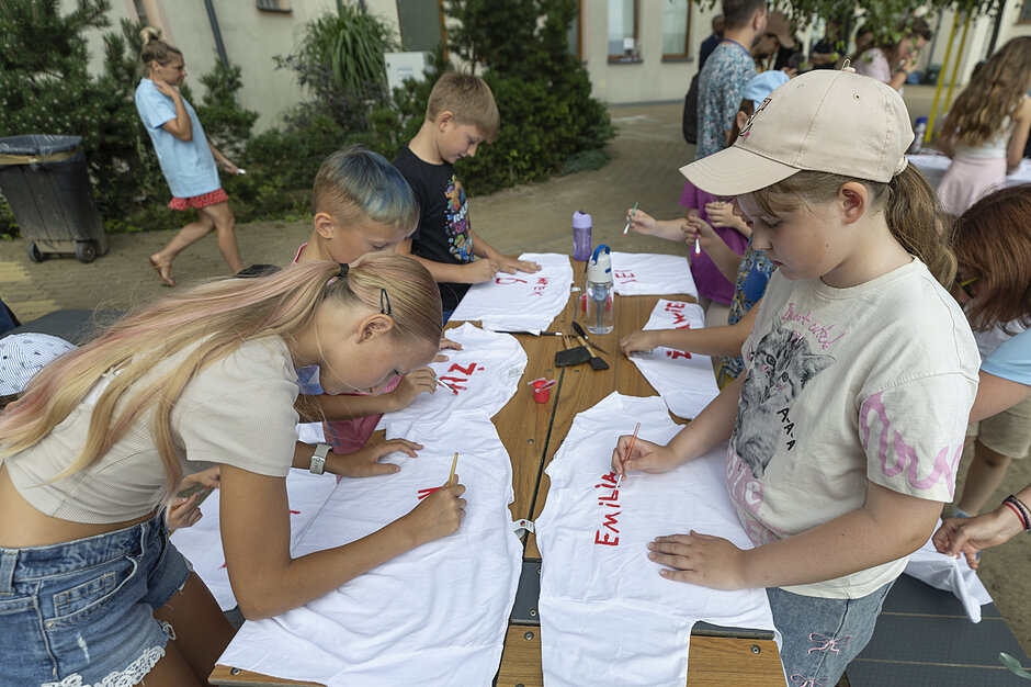 Akcja Lato 2026. Dzieci malują swoje imiona na białych koszulkach. 