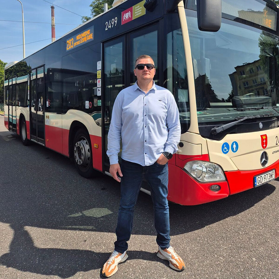 Zdjęcie mężczyzny, który pozuje do zdjęcia na tle autobusu miejskiego 