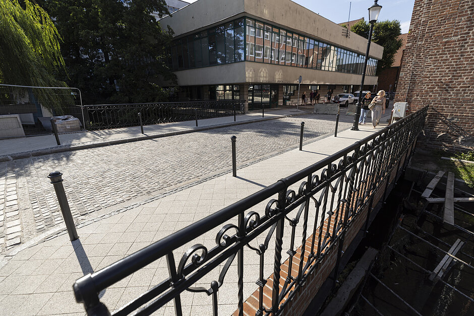 2zbliżenie na czarną balustradę mostu, widać też odnowioną brukowaną jezdnię i estetyczne jasne chodniki