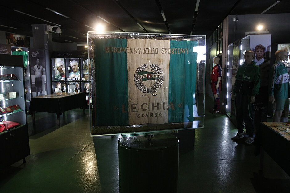 wyświetlacz w muzeum lub wystawie. Wyświetlacz wykonany jest ze szkła i ma zielone tło z banerem w środku, który brzmi Budowlany Klub Sportowy  i  Lechia Gdańsk . Baner ma również emblemat herbu ze słowem  Lechia  napisanym nad nim. Po prawej stronie wyświetlacza znajduje się kilka manekinów w zielono-białych koszulach piłkarskich. 