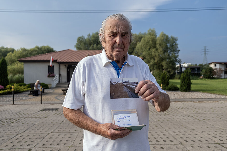 Starszy mężczyzna pokazuje do aparatu zdjęcie na działkach.