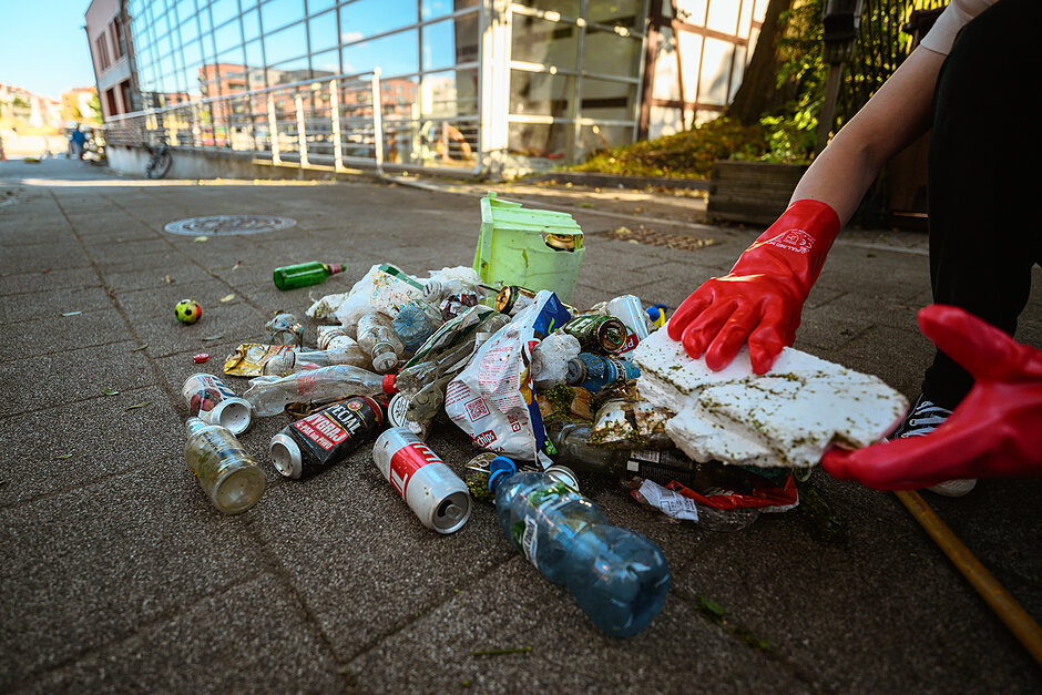 Rece w rękawicach sortują śmieci wysypane na chodnik. 