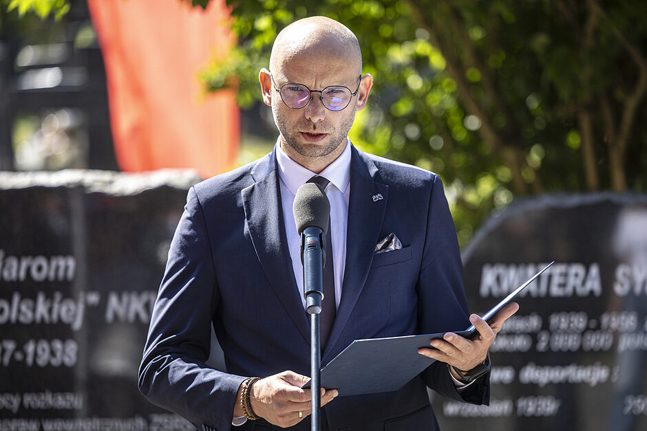 na zdjęciu piotr kryszewski w ciemnym garniturze, mówi do mikrofonu