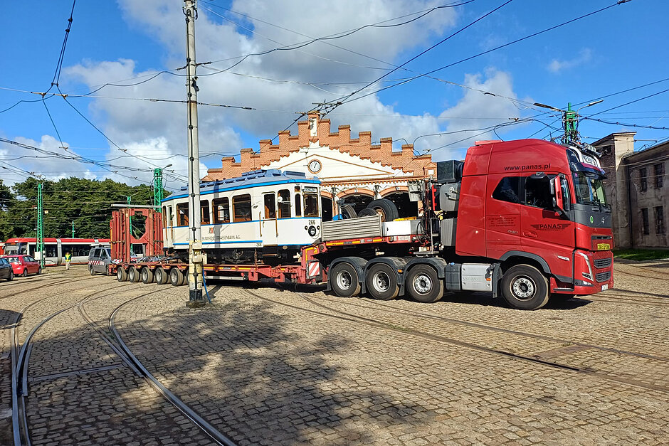 Zabytkowy tramwaj na przyczepie ciągnika siodłowego na terenie zajezdni tramwajowej.