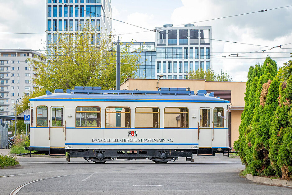 Zabytkowy tramwaj stoi na terenie zajezdni tramwajowej, w tle nowoczesne budynki.
