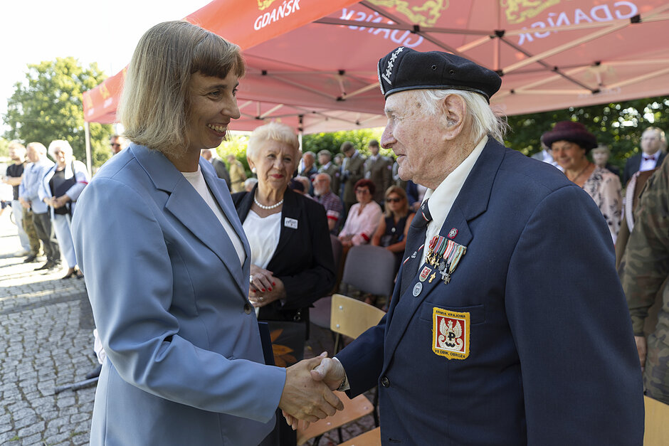 na zdjęciu kobieta w jasnoniebieskiej marynarce wita starszego mężczyznę w mundurze żołnierskim