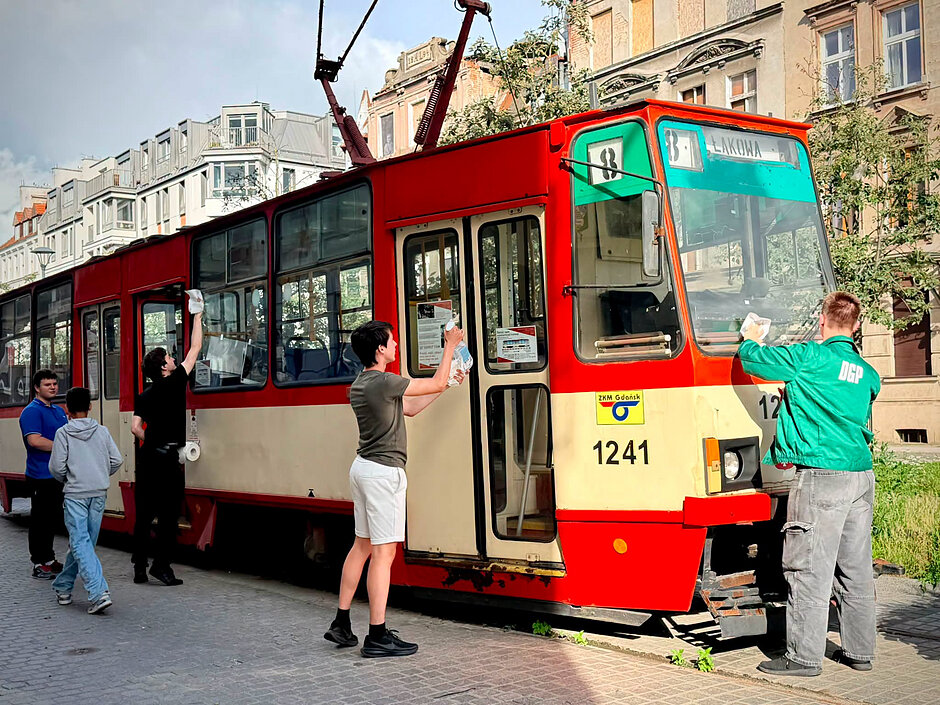 Kilka osób czyści stary tramwaj zaparkowany w starej dzielnicy miasta.