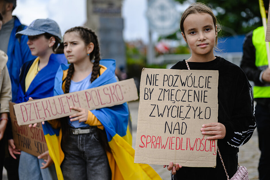 na zdjeciu młoda dziewczynka trzymająca szary karton z napisem, obok stoi inna dziewczynka