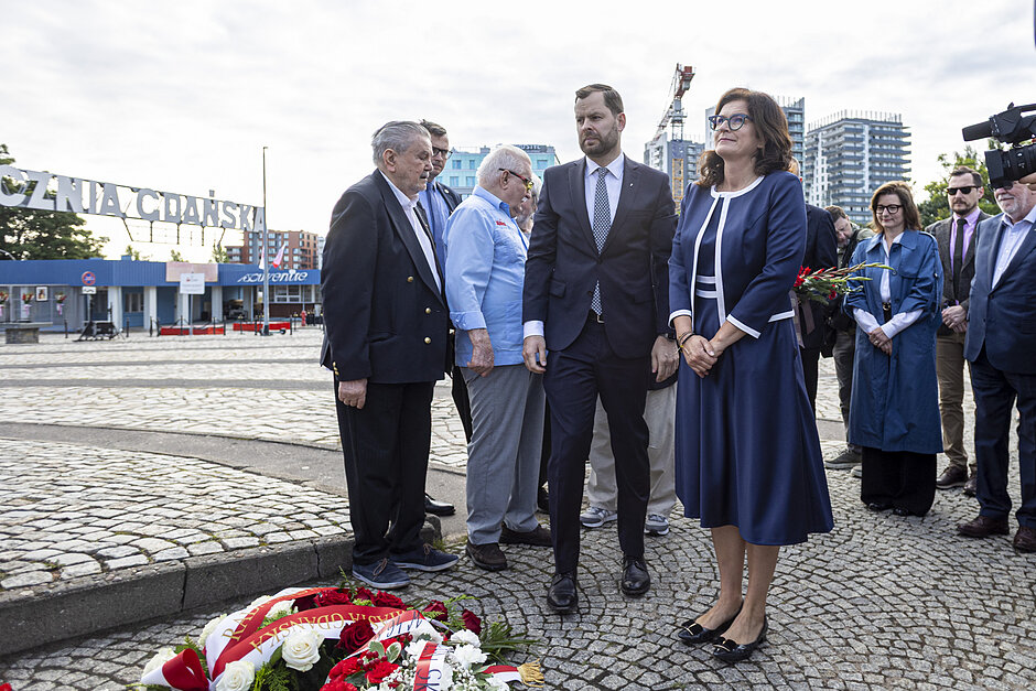 Kilka osób składa kwiaty pod pomnikiem.
