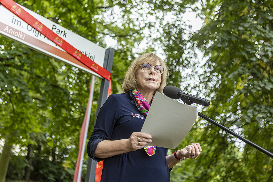 Wymieniona osoba przemawia pod tablicą z napisem Park im.Olgi Krzyżanowskiej 