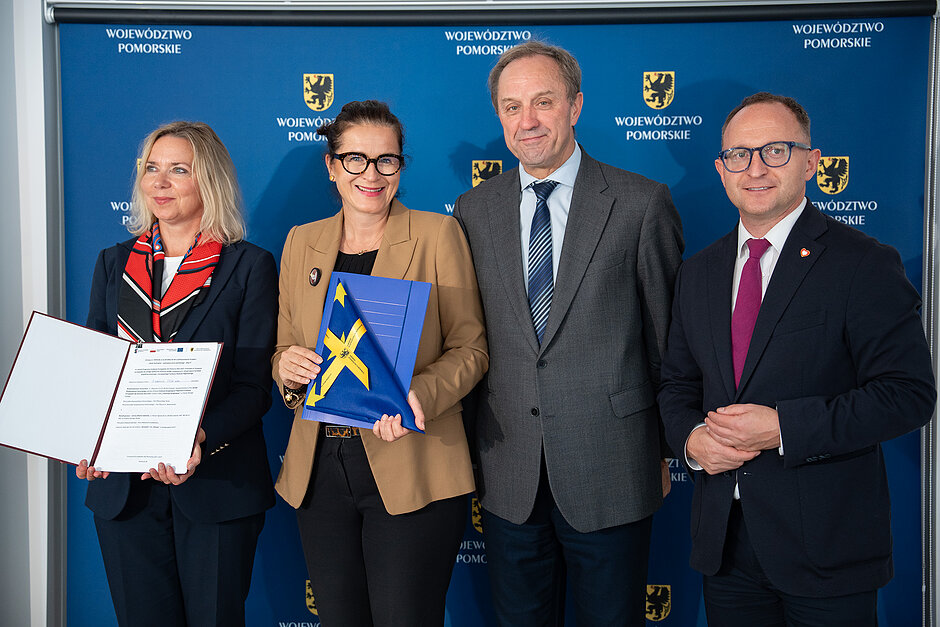 do zdjęcia pozują dwie kobiety i dwóch mężczyzn w średnim wieku, wszyscy w oficjalnych garniturach