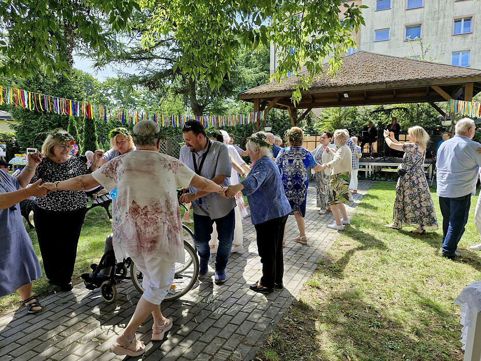 Seniorzy tańczą w ogrodzie podczas imprezy.