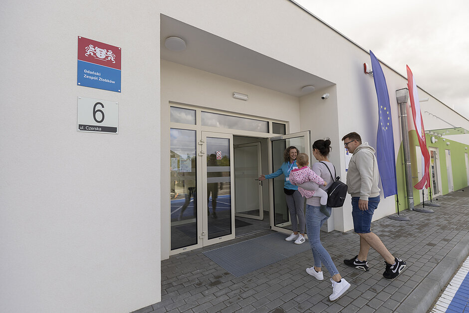 Kobieta w drzwiach żłobka wita rodziców z dzieckiem.