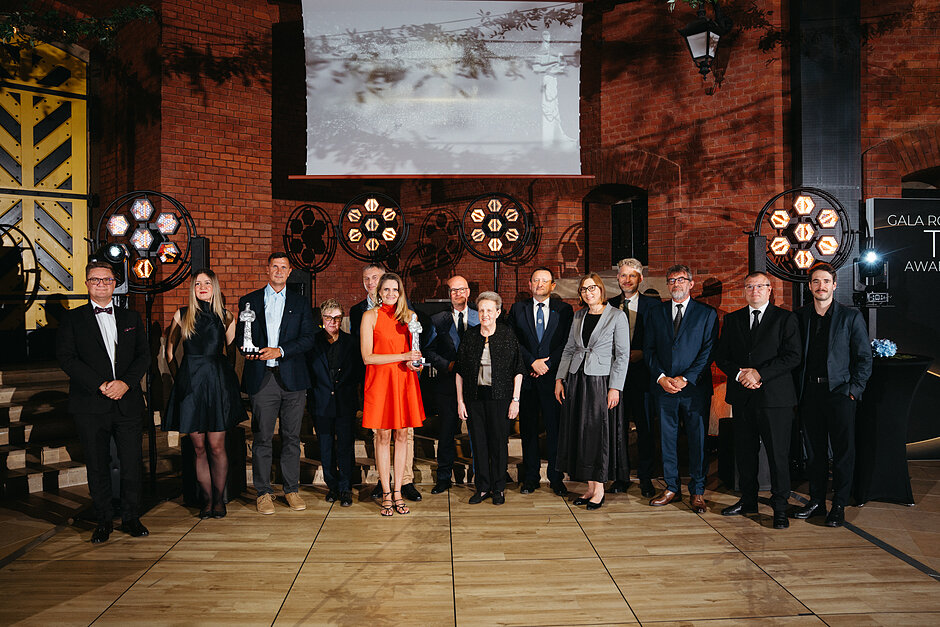 Kilkanaście osób odświętnie ubranych pozuje do zdjęcia, niektóre osoby trzymają statuetki.