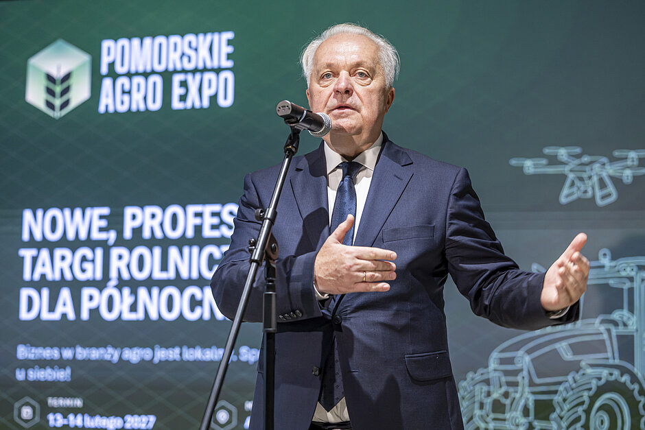 Mężczyzna mówi do mikrofonu podczas konferencji prasowej, Za nim ekran z napisami i grafikami.