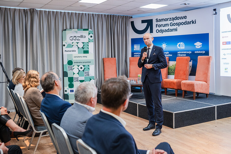 Mężczyzna przemawia do osób zebranych w sali konferencyjnej.