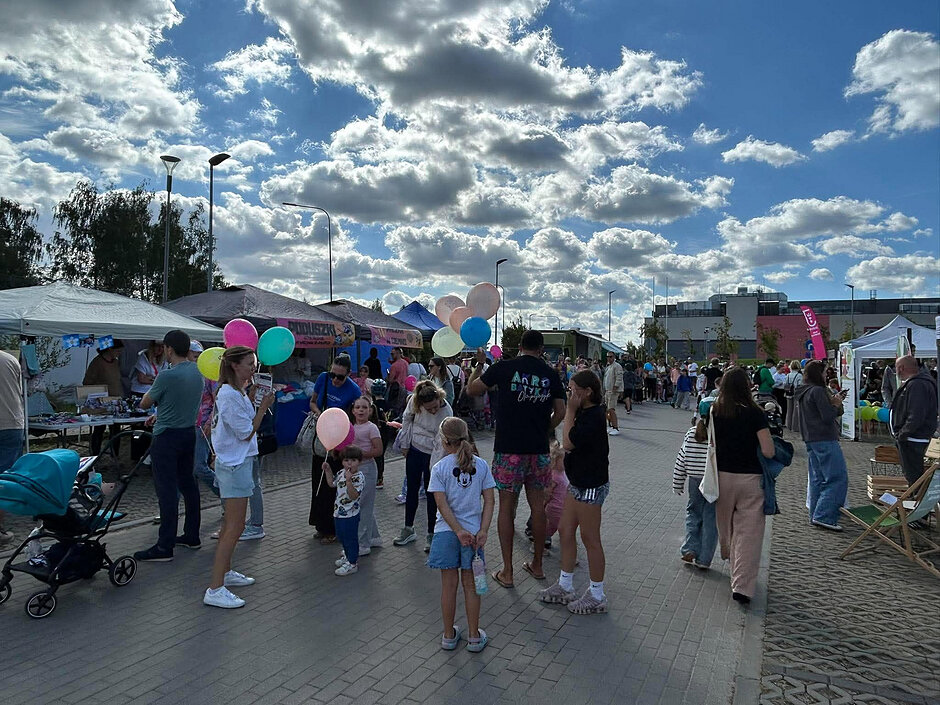 na zdjęciu dzieci stojące na zamkniętej ulicy, każde z balonikiem, jest też trochę dorosłych, widać trwający festyn