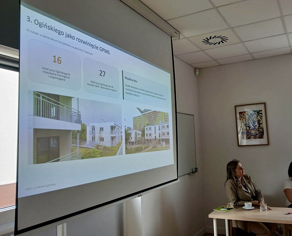 Zdjęcie przedstawia wnętrze sali i ekran, na którym wyświetlana jest prezentacja projektu