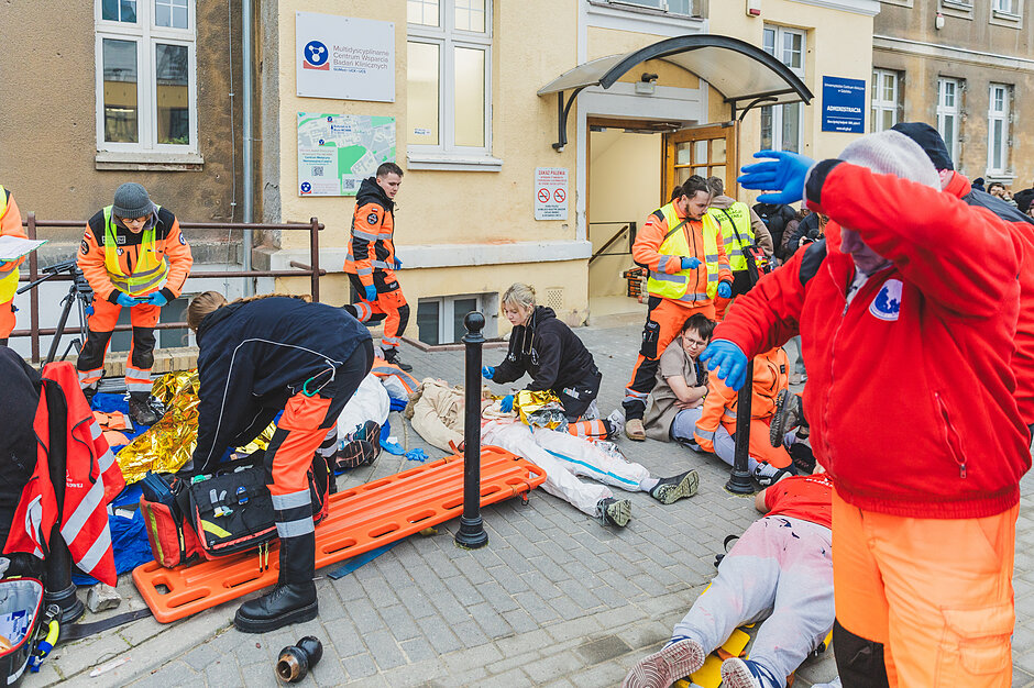 Pozoracja do ataku dronowego. Na ziemi leżą ranni. Dookoła nich pracują służby. 