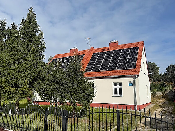 Wyremontowany budynek przy Łowickiej. Jasno otynkowany budynek z czerwoną dachówką. Na dachu są zamocowane panele fotowoltaiczne