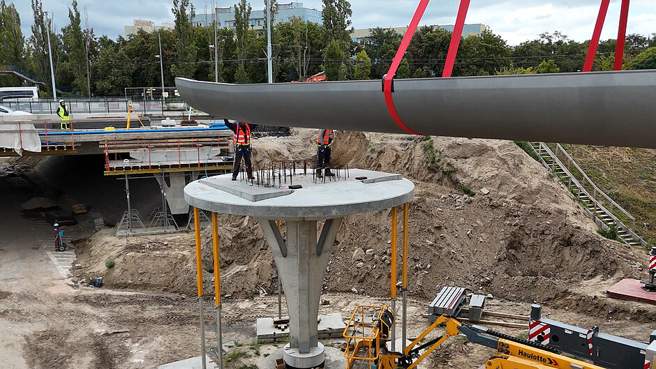 robotnicy stoją na podporze, łapią podawany im przez dźwig stalowy element