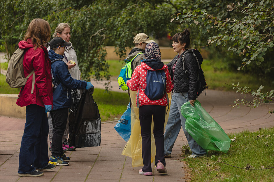 Trójka uczniów i trójka nauczycielek z workami na śmieci w parku miejskim.