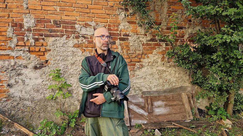 Fotograf z przewieszonym aparatem na tle ceglanej ściany