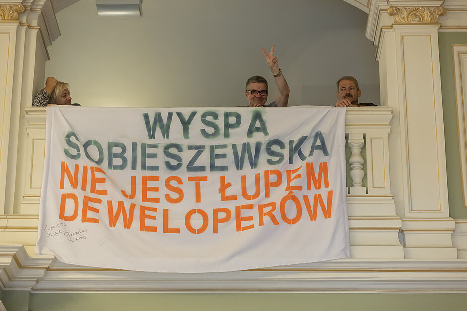 na zdjęciu dwóch mężczyzn i kobieta stoją za dużym białym transparentem z napisem wyspa sobieszewska nie jest łupem deweloperów