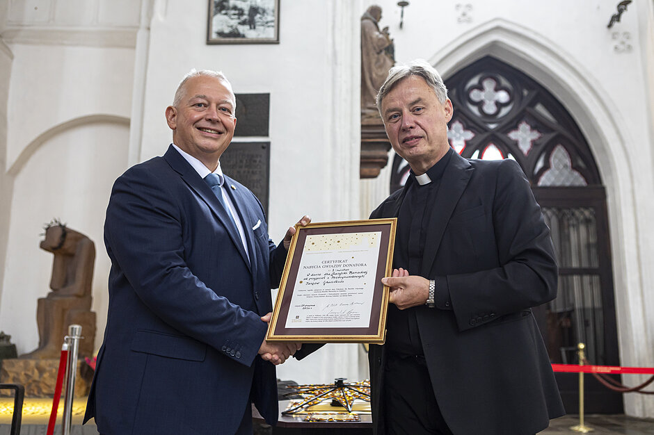 Dwóch mężczyzn trzymają certyfikat i podają sobie dłonie