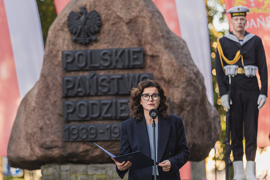 na zdjęciu prezydent gdańska na tle pomnika w postaci głazu z czarnym napisem polskie państwo podziemne, prezydent przemawia przy mikrofonie