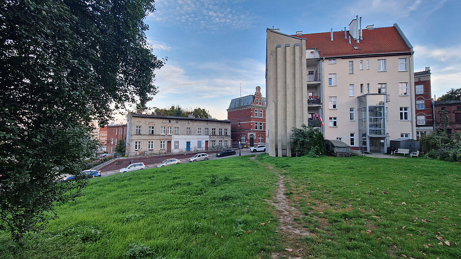 Widok na ulicę Biskupią: tyły wysokiej wyremontowanej kamienicy, a z lewej strony jednopiętrowy podłużny budynek do remontu 