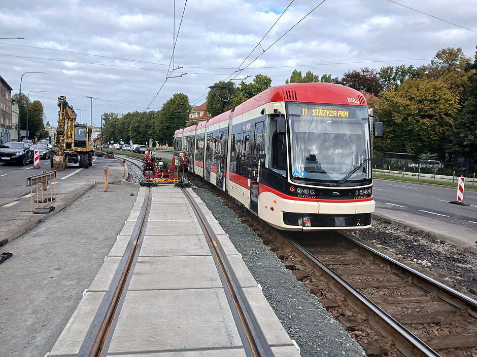 na zdjęciu po lewej wyremontowane betonowe torowisko tramwajowe, po prawej jeszcze stare wysłużone z drewnianym podkładem, po nich jedzie biało czerwony tramwaj
