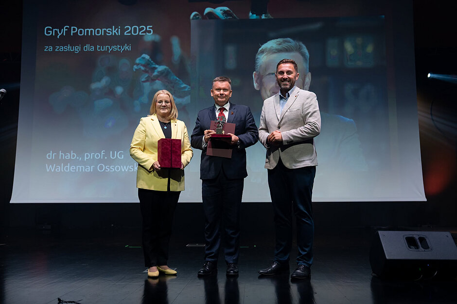 Kobieta i dwóch mężczyzn na scenie z nagrodami.