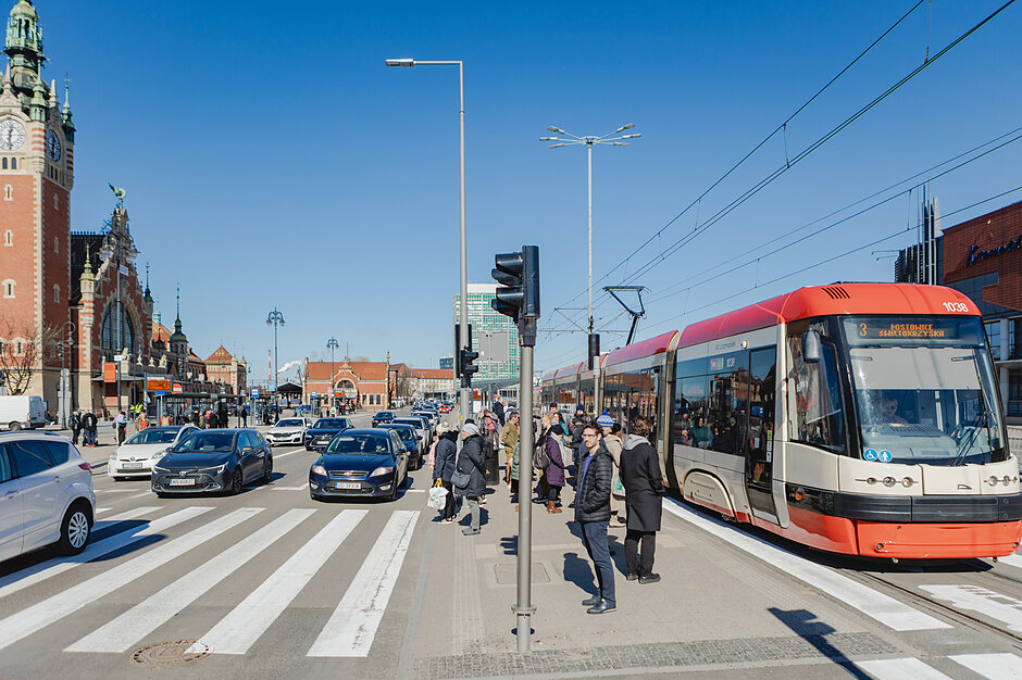 Przystanki tramwajowe, piesi stoją na przejściu dla pieszych, samochody jadą