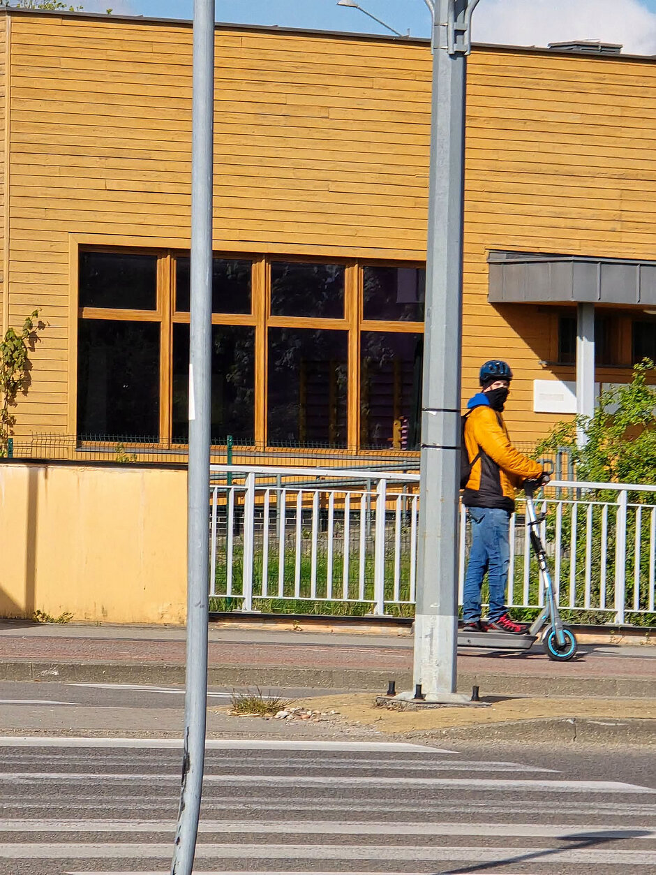 Mężczyzna w kominiarce i kasku jadący na hulajnodze elektrycznej
