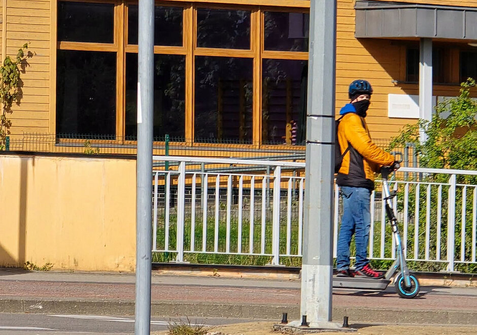 Mężczyzna w kominiarce i kasku jadący na hulajnodze elektrycznej