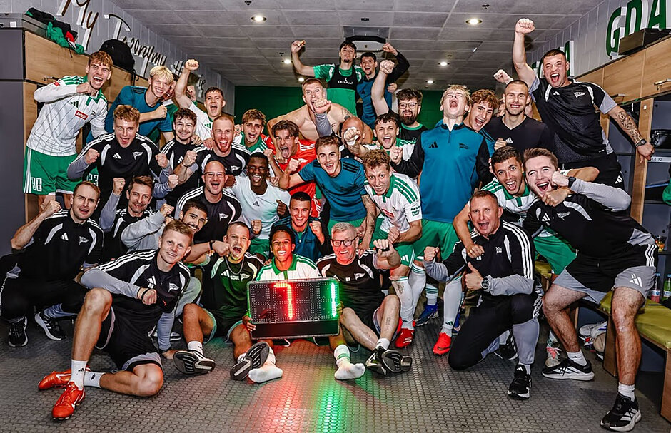 Grupa ponad 20 tryumfujących mężczyzn w strojach sportowych pozuje do wspólnego zdjęcia