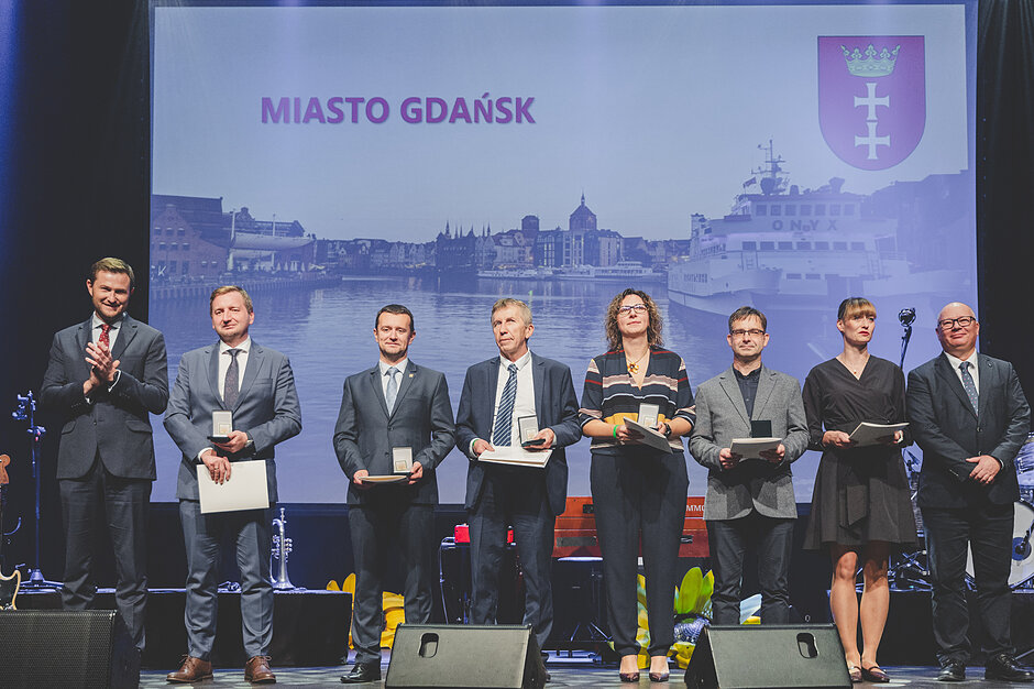 Osiem osób stojących rzędem na scenie, jedna obok drugiej