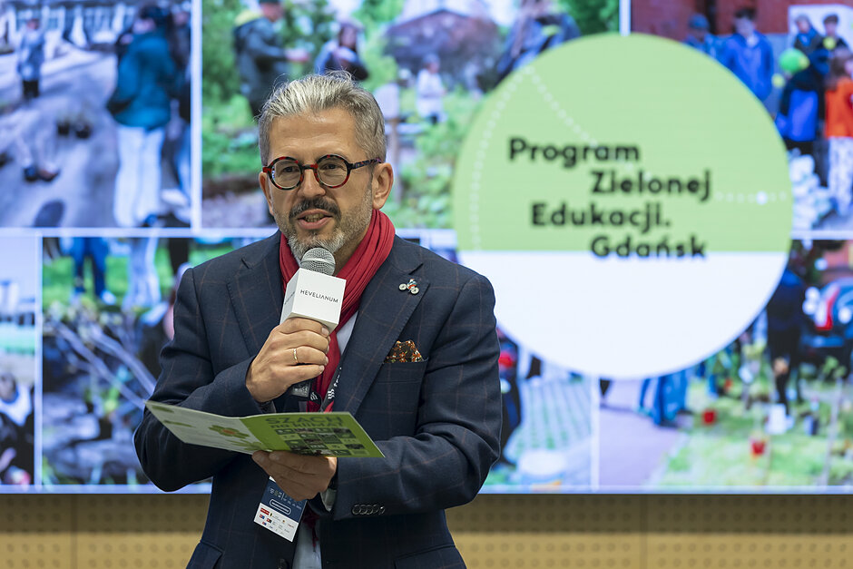mężczyzna na tle kolażu zdjęć z opisem program zielonej edukacji, mówi do mikrofonu