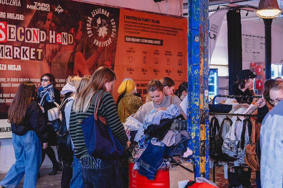 Ludzie oglądają ubrania. W tle baner second hand marketu