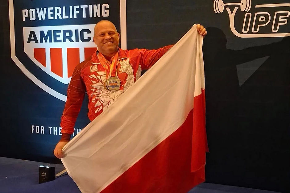 Marcin trzyma polską flagę i uśmiecha się do aparatu