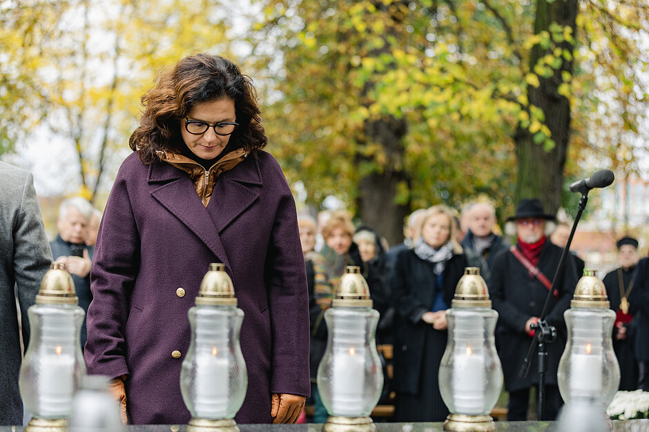 Prezydent Aleksandra Dulkiewicz w pozycji ukłonu przed centralnym pomnikiem cmentarza nieistniejących cmentarzy