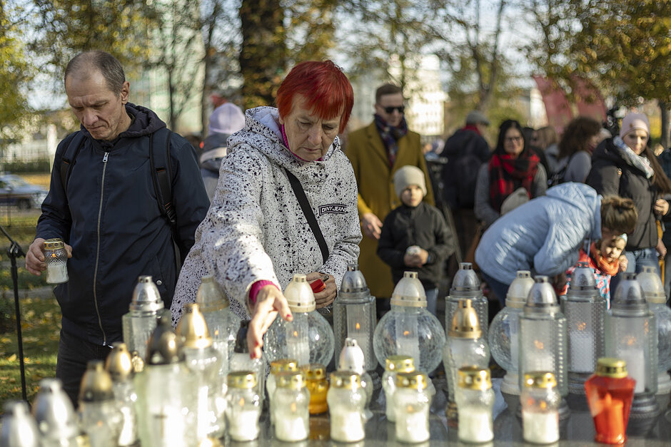 Wiele osób stawia zapalone znicze cmentarne na dużej marmurowej płycie 