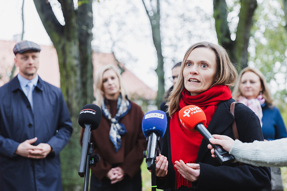 na zdjęciu miejska konserwator zabytków, mówi do mikrofonów dziennikarskich, w tle za nią stoi kilka osób